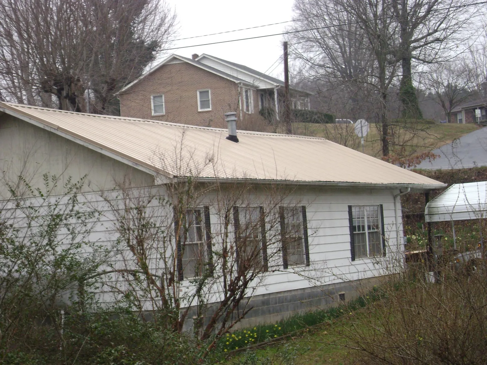 Tan metal roof on a white sided house set into a hillside — Commercial Roofing by Roofing Brothers in Merritt Island